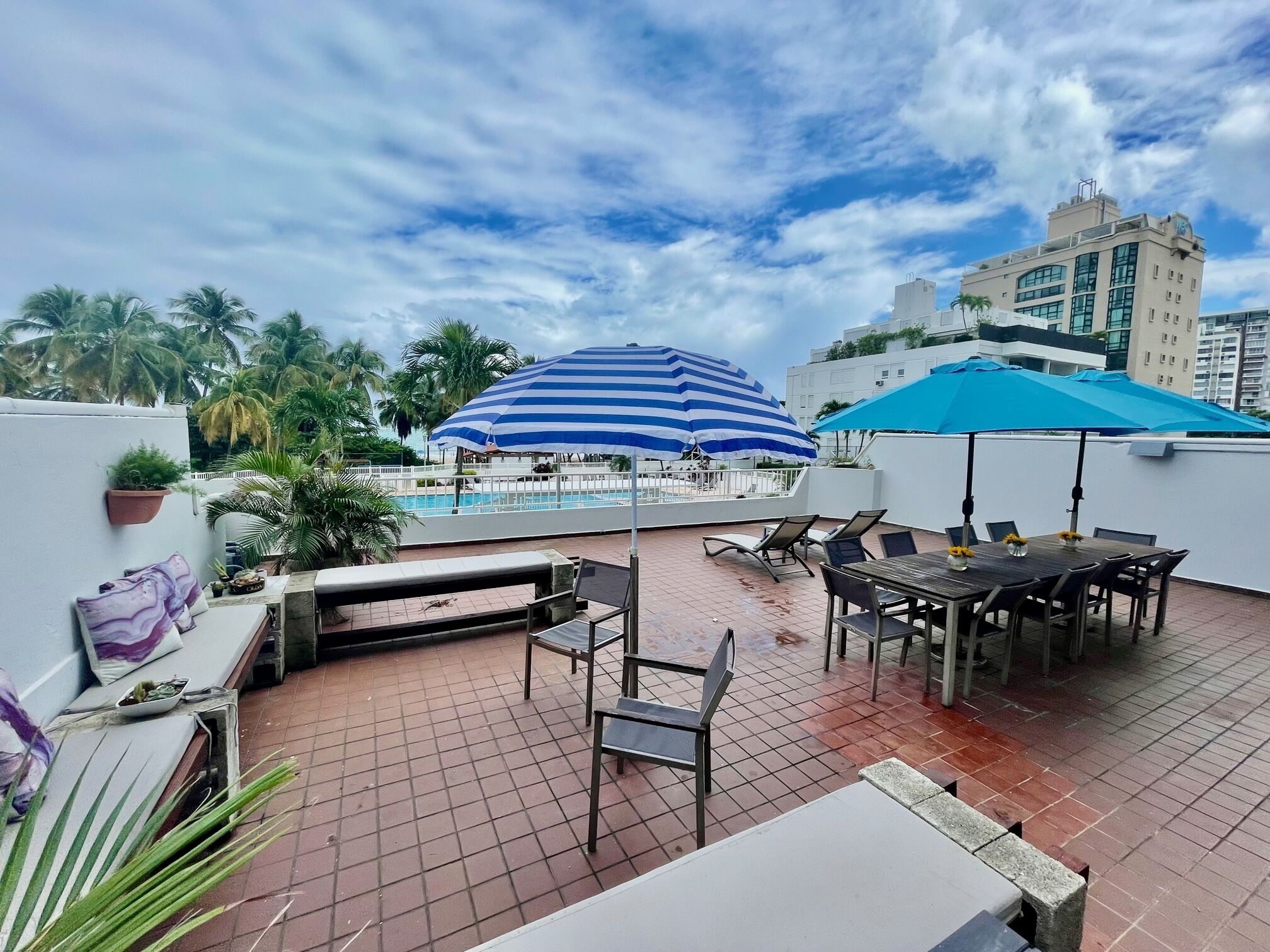 A rooftop terrace with a pool, lounge chairs, and umbrellas.