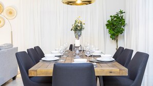 Un coin repas avec une table en bois dressée pour six personnes, entourée de chaises sombres, avec une suspension au-dessus et une plante en pot sur le côté.