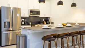 Une cuisine moderne dotée d’appareils électroménagers en acier inoxydable, d’un îlot central avec des tabourets de bar et d’un éclairage suspendu.