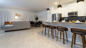 Une cuisine moderne avec des meubles blancs, un réfrigérateur en acier inoxydable et un coin bar équipé de tabourets.