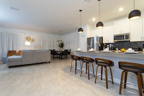A modern kitchen with white cabinets, a stainless steel refrigerator, and a bar area with stools.