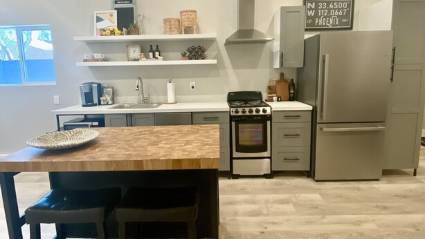 Una cocina moderna con una mesa y sillas de madera, electrodomésticos integrados y un cartel con la dirección.