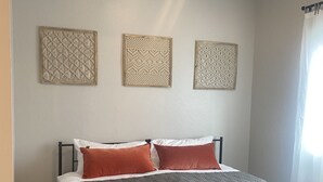 Un dormitorio con cama, almohadas y tres paneles decorativos en la pared.