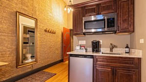 A kitchen with wooden cabinets, a stainless steel microwave, a dishwasher, and a countertop with various appliances. - 124 Lofts #2 - Downtown Dundee - Walk to Dining (West Dundee)