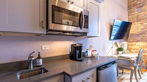 A modern kitchen with stainless steel appliances, a built-in microwave, a coffee maker, and a small dining area with a chair and table. - 124 Lofts #3 - Downtown Dundee - Walk to Dining (West Dundee)