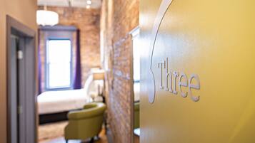 A hotel interior with a bed, a chair, and a wall with the word 'three' visible.