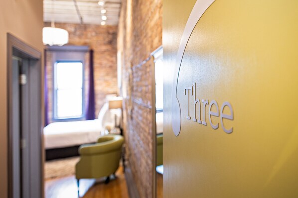 A hotel interior with a bed, a chair, and a wall with the word 'three' visible.
