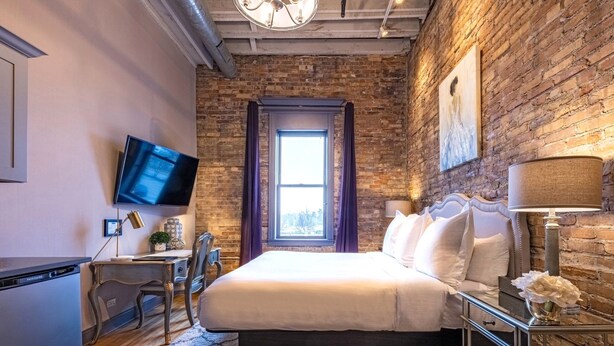 A bedroom with a brick wall, a bed, a desk, a TV, and a window. - 124 Lofts #3 - Downtown Dundee - Walk to Dining (West Dundee)