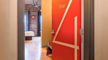 A hallway leading to a bedroom with a red door labeled 'Four,' wooden flooring, a bed, and a ceiling fan.