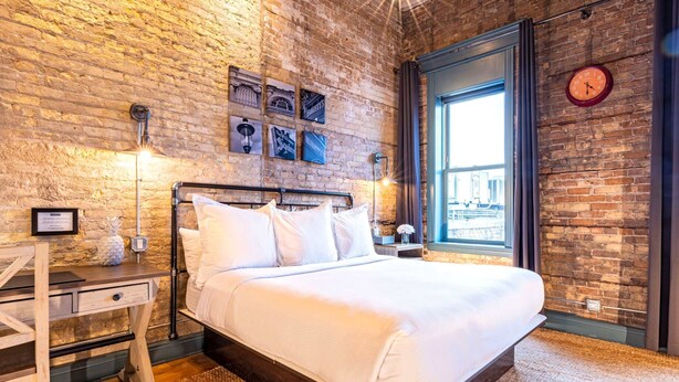 A bedroom with a brick wall, a bed, a desk, and a window with a view. - 124 Lofts #4 - Downtown Dundee - Walk to Dining (West Dundee)