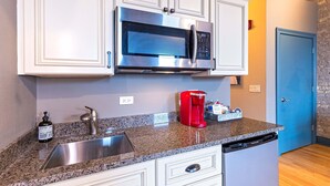 A kitchen with white cabinets, a stainless steel sink, a granite countertop, a red coffee maker, and a dishwasher. - 124 Lofts #4 - Downtown Dundee - Walk to Dining (West Dundee)