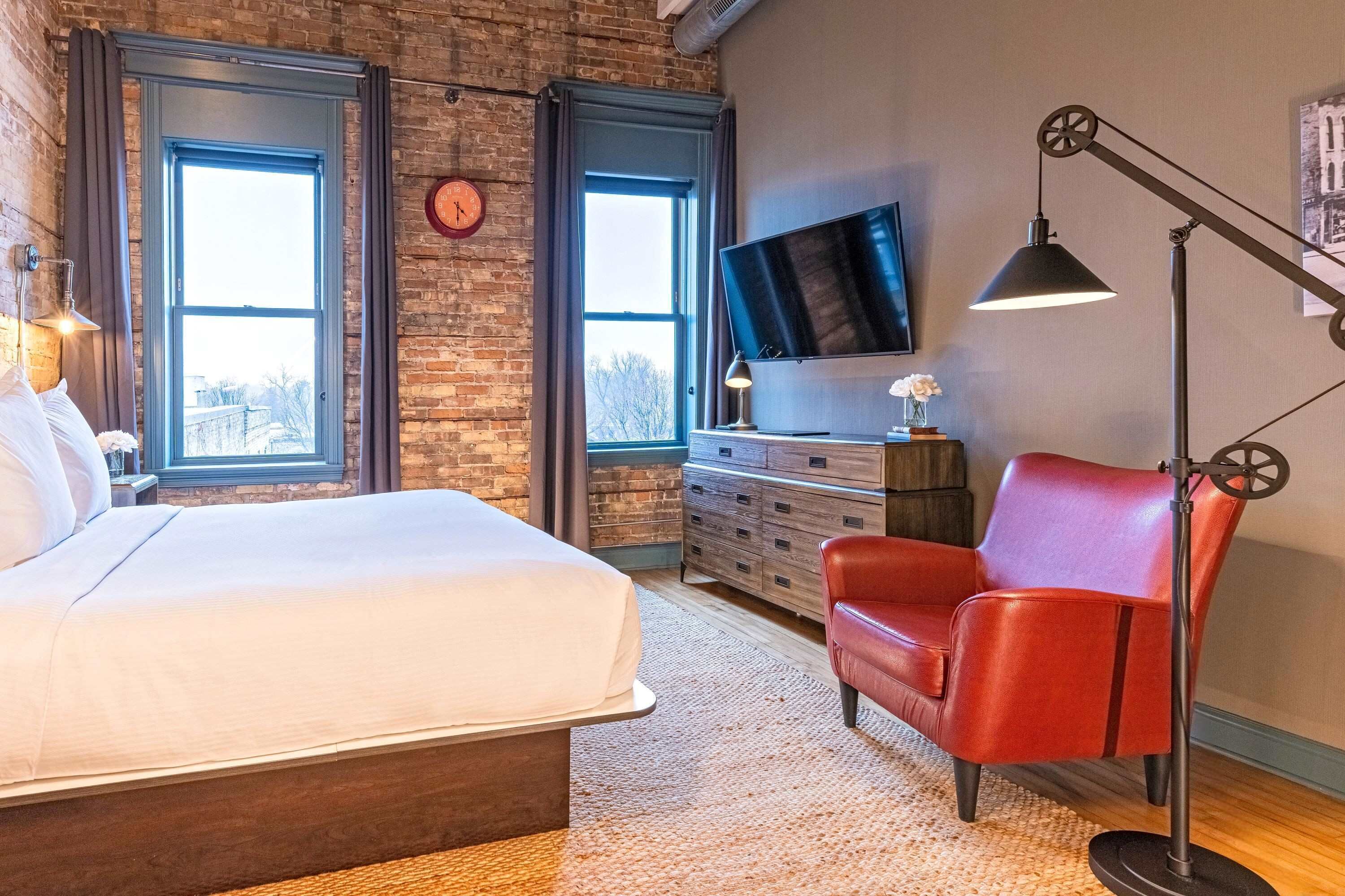 A bedroom with a bed, a red chair, a TV, and a clock on the wall.