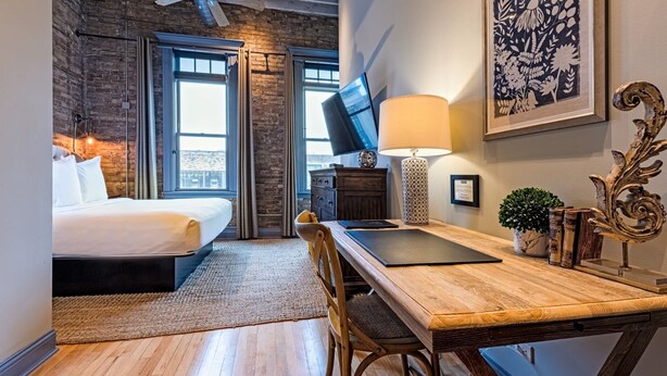 A hotel room with a bed, a desk, a lamp, a TV, and a framed artwork. - 124 Lofts #1 - Downtown Dundee - Walk to Dining (West Dundee)