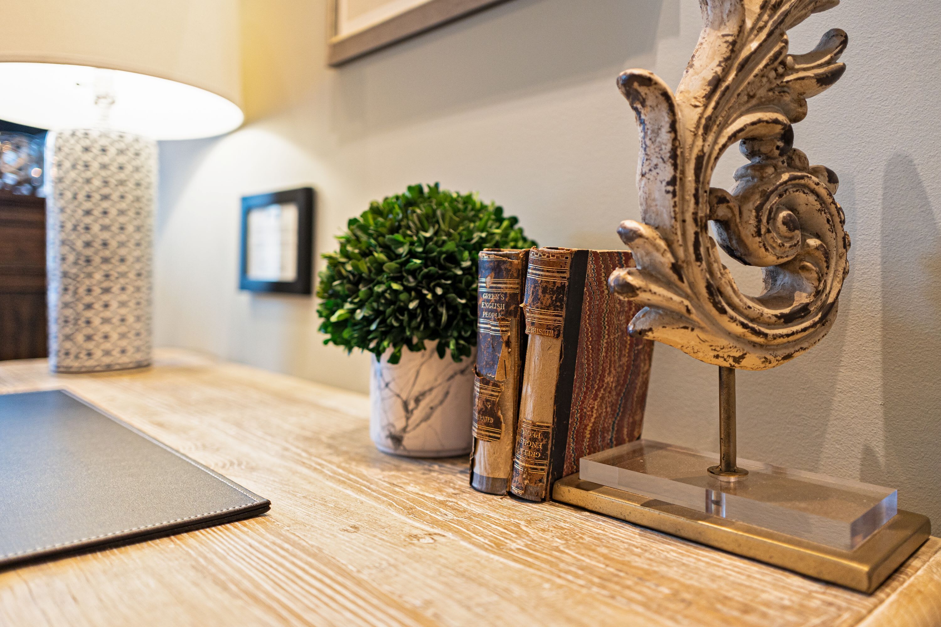 Una mesa de madera con una lámpara, una planta en maceta y un atril decorativo con libros.