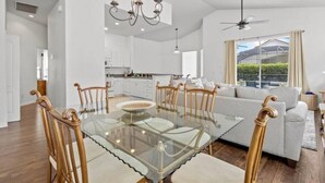 Amplia sala de estar con una mesa de comedor de vidrio, sillas de madera, un sofá y un ventilador de techo.