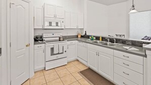 Una cocina moderna con armarios blancos, horno empotrado, microondas y lavaplatos.