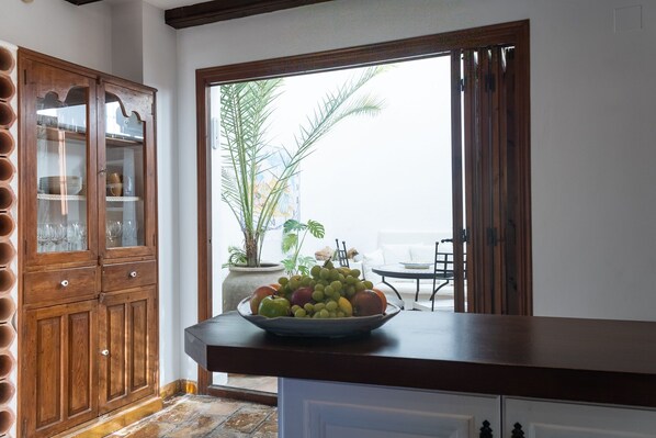 A kitchen with a wooden cabinet, a bowl of fruit on the counter, and a view of a balcony with a plant.