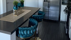 Une cuisine moderne avec un plan de travail noir, un réfrigérateur en acier inoxydable et des tabourets de bar bleus recouverts de tissu.