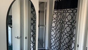 Un couloir avec un miroir, un rideau de douche à motifs et un tapis noir.