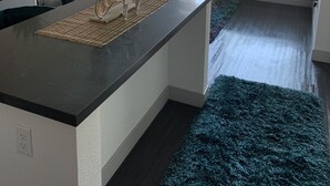 Une cuisine moderne dotée d’un îlot central, d’un coin repas avec un canapé de couleur turquoise et d’une grande fenêtre qui laisse entrer la lumière naturelle.