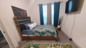 Une chambre à coucher avec un lit, des rideaux, un tableau, une télévision et une plante.