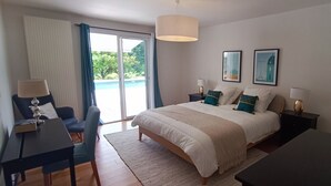 Une chambre moderne avec un grand lit, un bureau et une chaise. Une porte-fenêtre coulissante donne accès à un balcon.