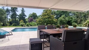 Une terrasse extérieure avec une piscine, entourée d’arbres et de verdure.