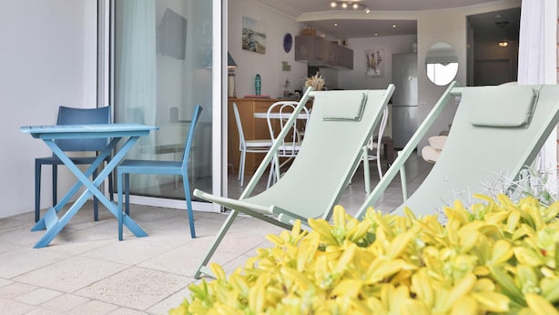 Une pièce dotée d’une porte vitrée donnant sur un balcon, d’une table à manger avec des chaises, et d’un coin cuisine visible à travers la porte.