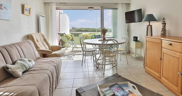 A living room with a sofa, a dining table with chairs, a TV, and a cabinet.