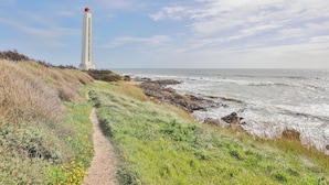 Un sentier côtier menant à un phare, avec une côte rocheuse et des vagues déferlant sur l’océan.