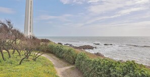 A coastal path with a tall white structure, possibly a lighthouse, and the ocean in the background.