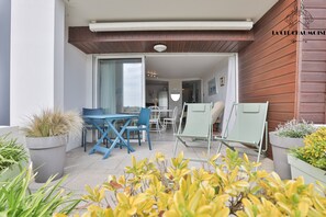 An outdoor patio area with a table and chairs, potted plants, and a sliding glass door leading to an interior space.