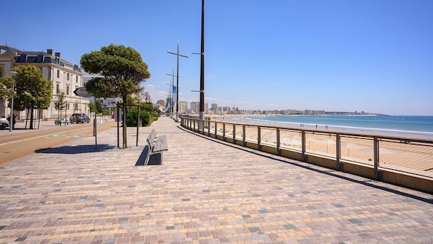 Une promenade dallée avec un banc, une plage et un ciel dégagé.