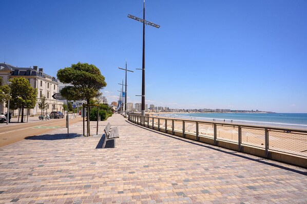 Eine gepflasterte Promenade mit einer Bank, einem Strand und einem klaren Himmel.