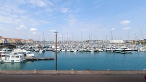 Un port de plaisance où sont amarrés de nombreux bateaux, un pont piétonnier et des bâtiments en arrière-plan.
