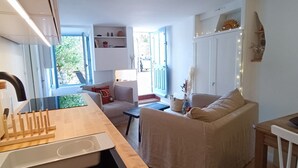 Ett kompakt bostadsutrymme med ett litet kök, en matplats och en sittgrupp med en soffa och en fåtölj.