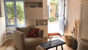 Ett mysigt vardagsrum med en soffa, ett soffbord och en bokhylla. Det finns ett fönster med blå ramar och utsikt över grönområden utanför.