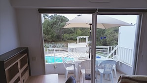 Un balcón con piscina, sillas blancas y una mesa.