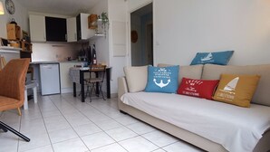 Ein modernes Wohnzimmer mit einer Couch, einem Essbereich mit Tisch und Stühlen sowie einer Küche mit Schränken und einem Kühlschrank.