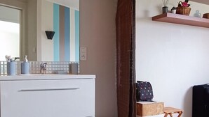 Ein modernes Badezimmer mit weißem Waschtisch, dunklem Holzboden, einer gestreiften Wand und einem Spiegel über dem Waschtisch.