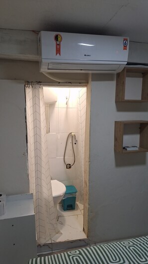 A small, narrow bathroom with a toilet, shower, and air conditioning unit mounted on the wall. - Pelourinho, entire house. (Salvador)
