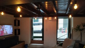 A room with a TV, a chair, a plant, and a view of the outside. - Pelourinho, complete house. (Salvador)