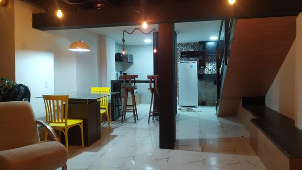 A spacious living area with a dining table, yellow chairs, and a kitchen in the background. - Pelourinho, complete house. (Salvador)