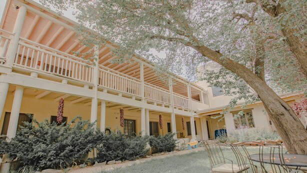 A building with a covered patio area, outdoor seating, and a large tree. - Upstairs Queen w/ shared balcony - 6 (Taos County)