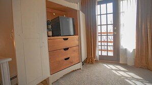 A room with a white wardrobe, a small refrigerator, and a sliding glass door with curtains. - Upstairs Queen w/ shared balcony - 6 (Taos County)