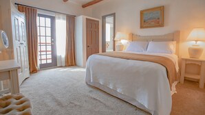 A bedroom with a large bed, two bedside lamps, a door, and a window with curtains. - Upstairs Queen w/ shared balcony - 6 (Taos County)