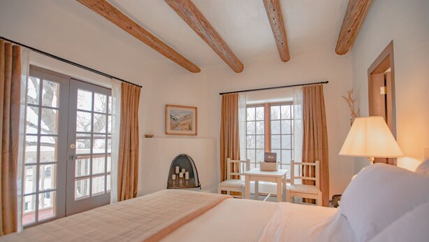 A hotel room with a large bed, a small table with a chair, and a window with curtains. - Upstairs Queen w/ private entrance - 4 (Taos County)