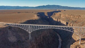 A steel bridge spanning a deep canyon with a clear sky and distant mountains.