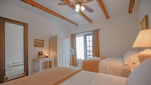 A hotel room with two beds, a ceiling fan, a desk with a lamp, and a window with curtains.