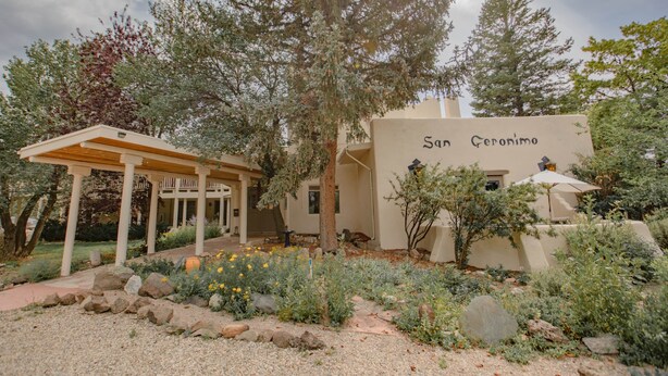 A building with the name 'San Geronimo' on its facade, surrounded by a garden with various plants and a pergola structure.